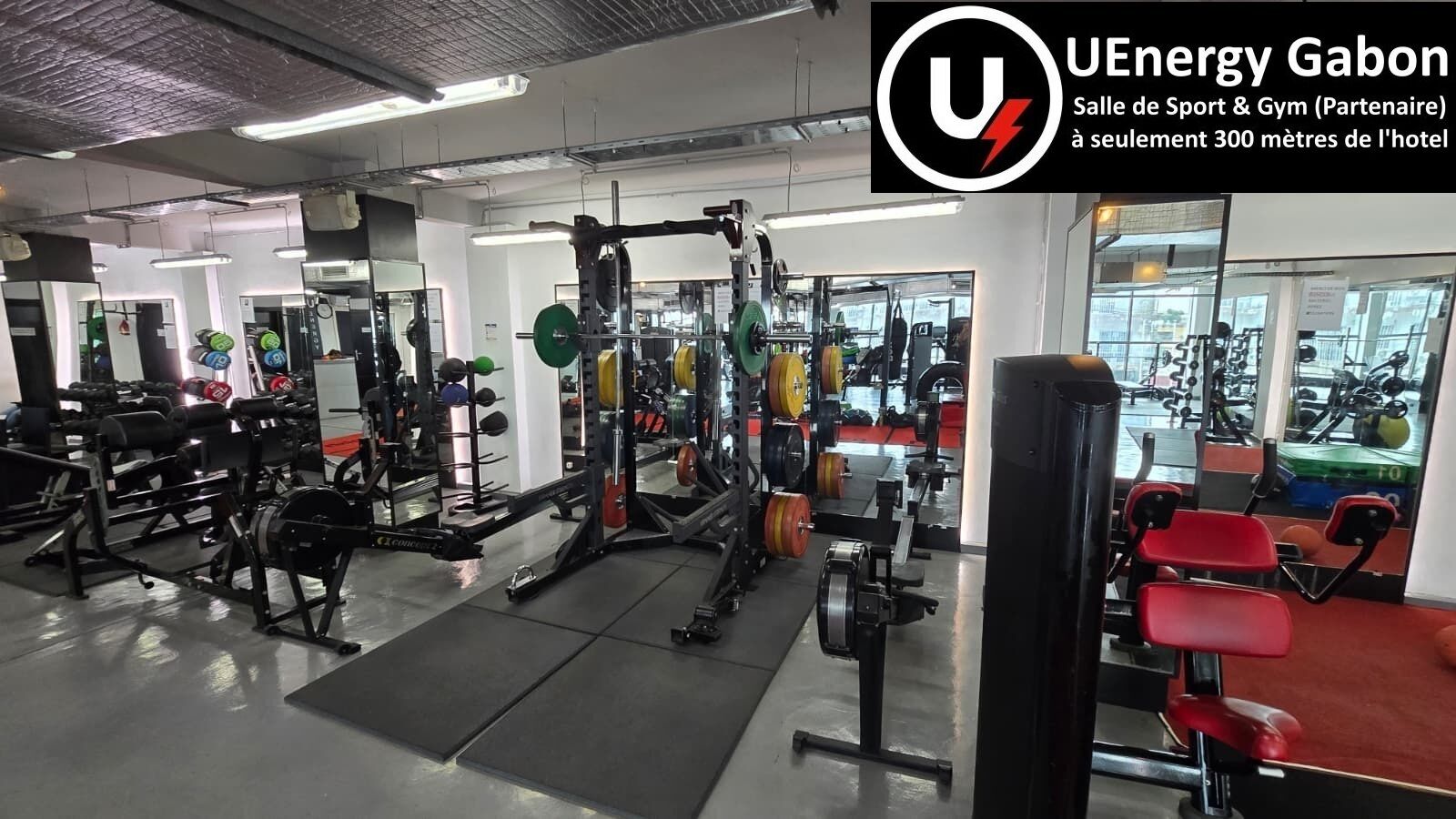 Un gimnasio con equipamiento de levantamiento de pesas, espejos y sillas de ejercicio rojas.