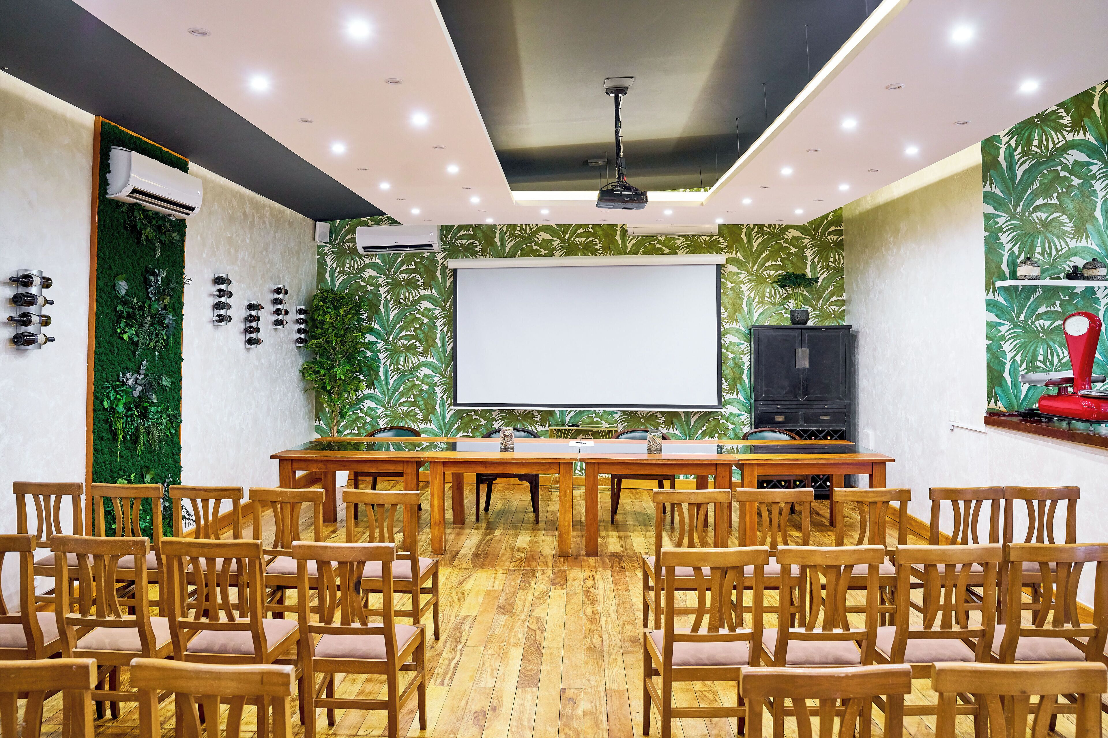 Un salón de conferencias con una gran mesa y sillas, una pantalla de proyector y una pared cubierta de plantas verdes.