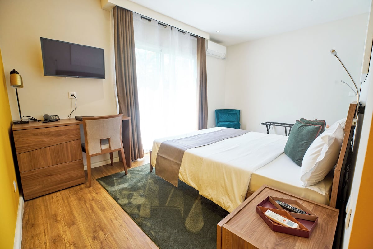 Ein Hotelzimmer mit Bett, Schreibtisch, Stuhl, Fernseher und einem Fenster mit Vorhängen.