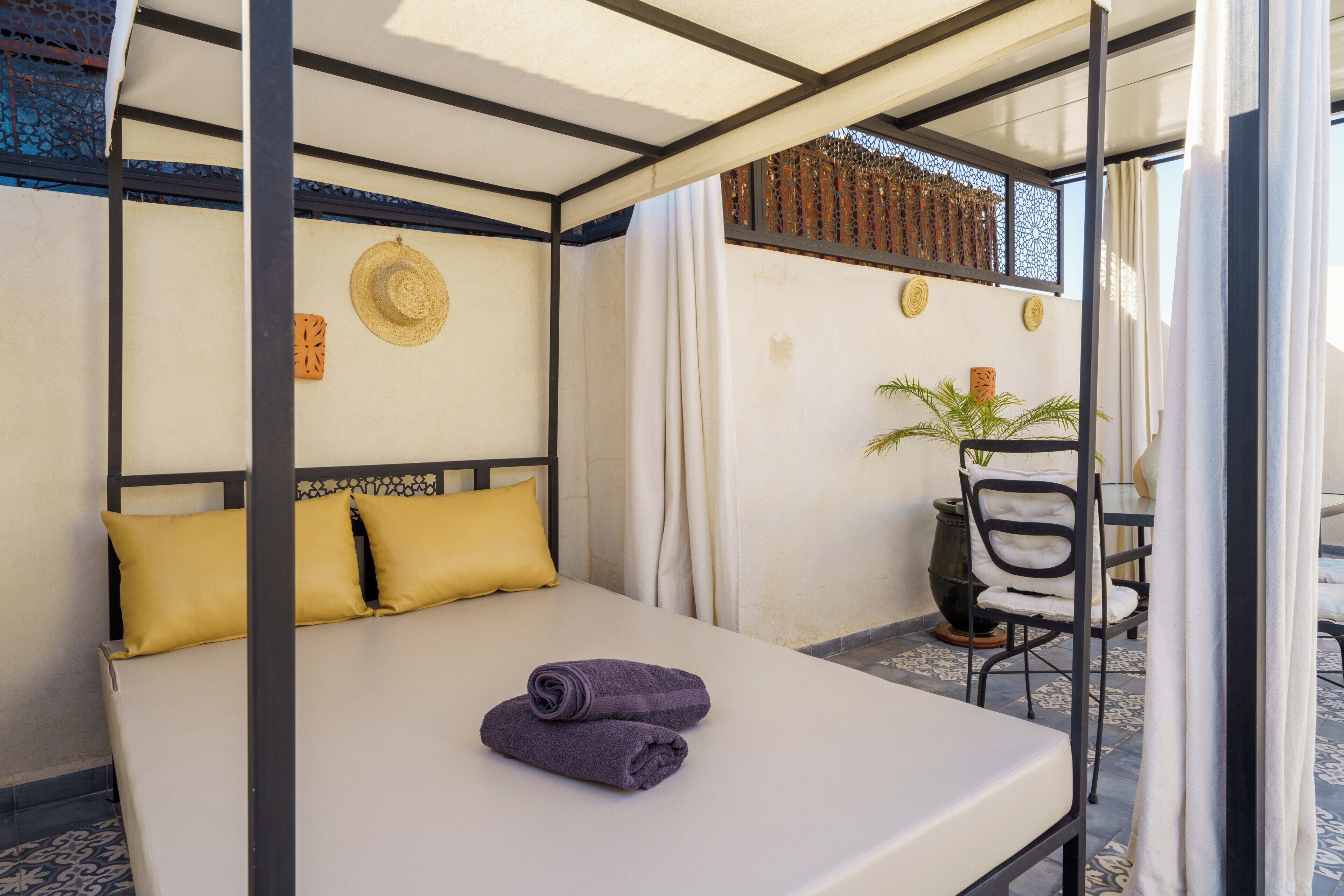 A neatly made bed with two pillows, a pair of rolled towels, and a small table with a chair.