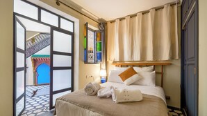 Habitación de hotel con cama, mesita de noche, lámpara y vista a un arco azul a través de una puerta abierta.
