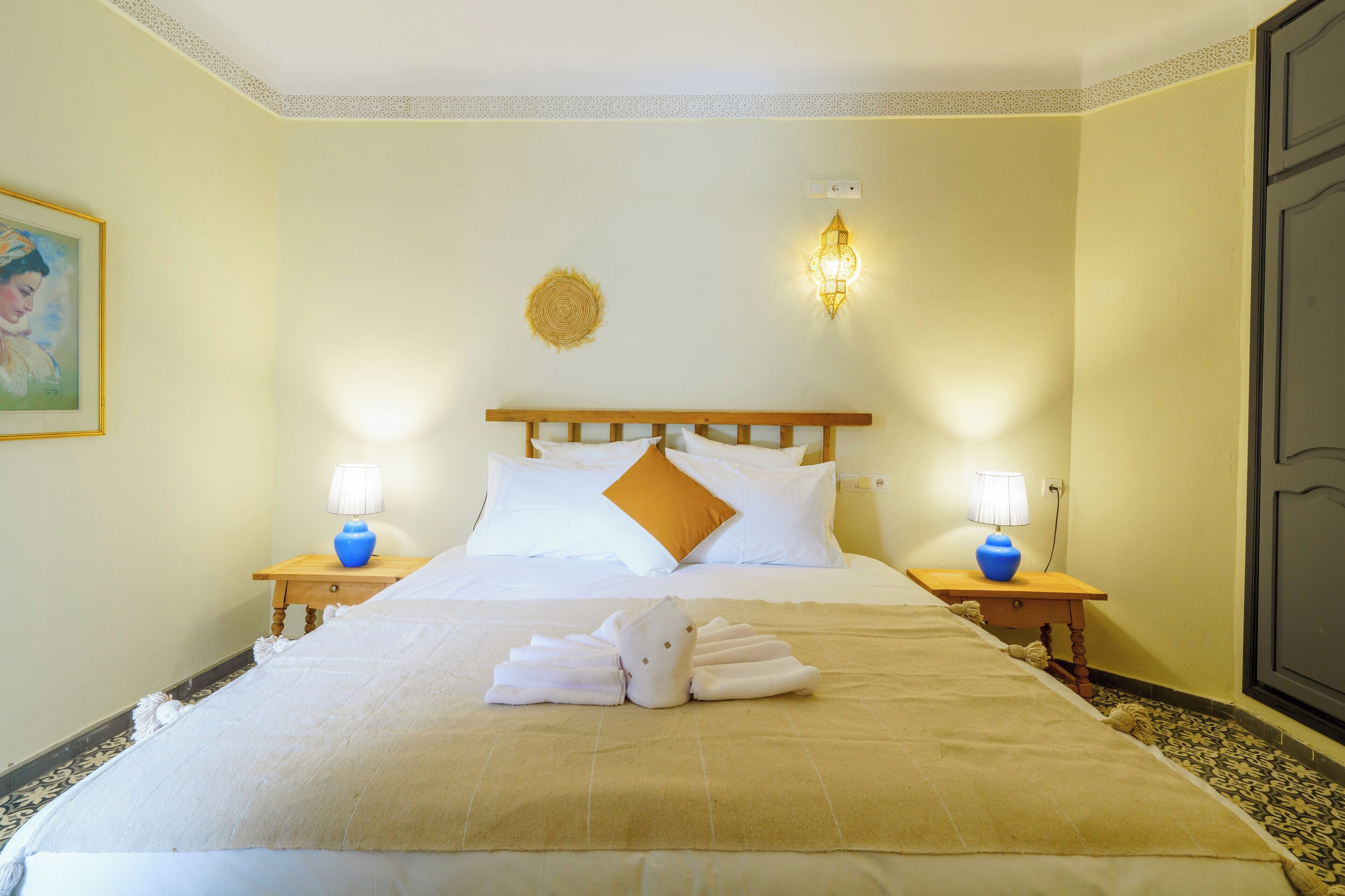 Ein Hotelzimmer mit einem ordentlich bezogenem Bett, zwei Nachttischlampen, einer Wandleuchte und einem gerahmten Bild an der Wand.