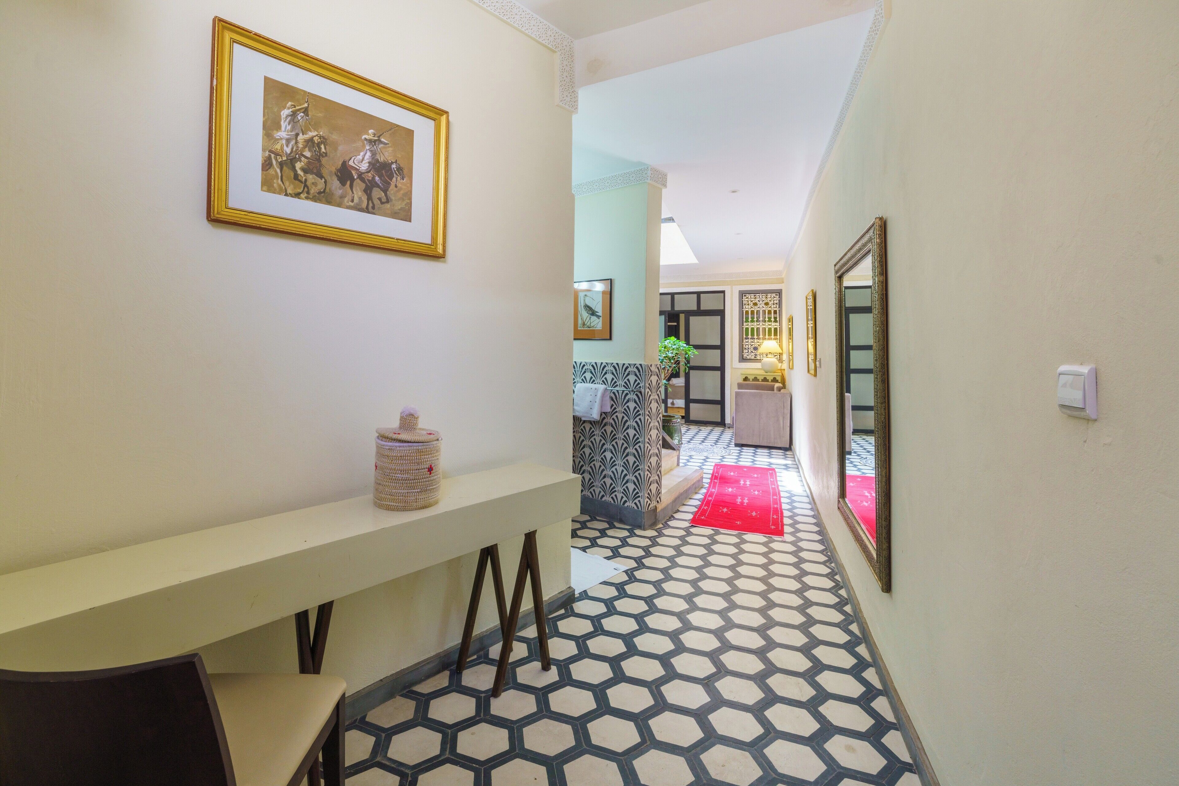 A hallway with patterned flooring, a bench, a framed picture on the wall, and a red rug.