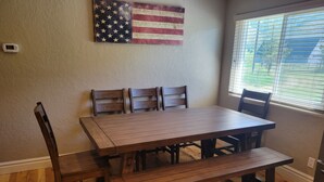 Un comedor con una mesa y sillas de madera, un banco y una bandera estadounidense colgada en la pared.