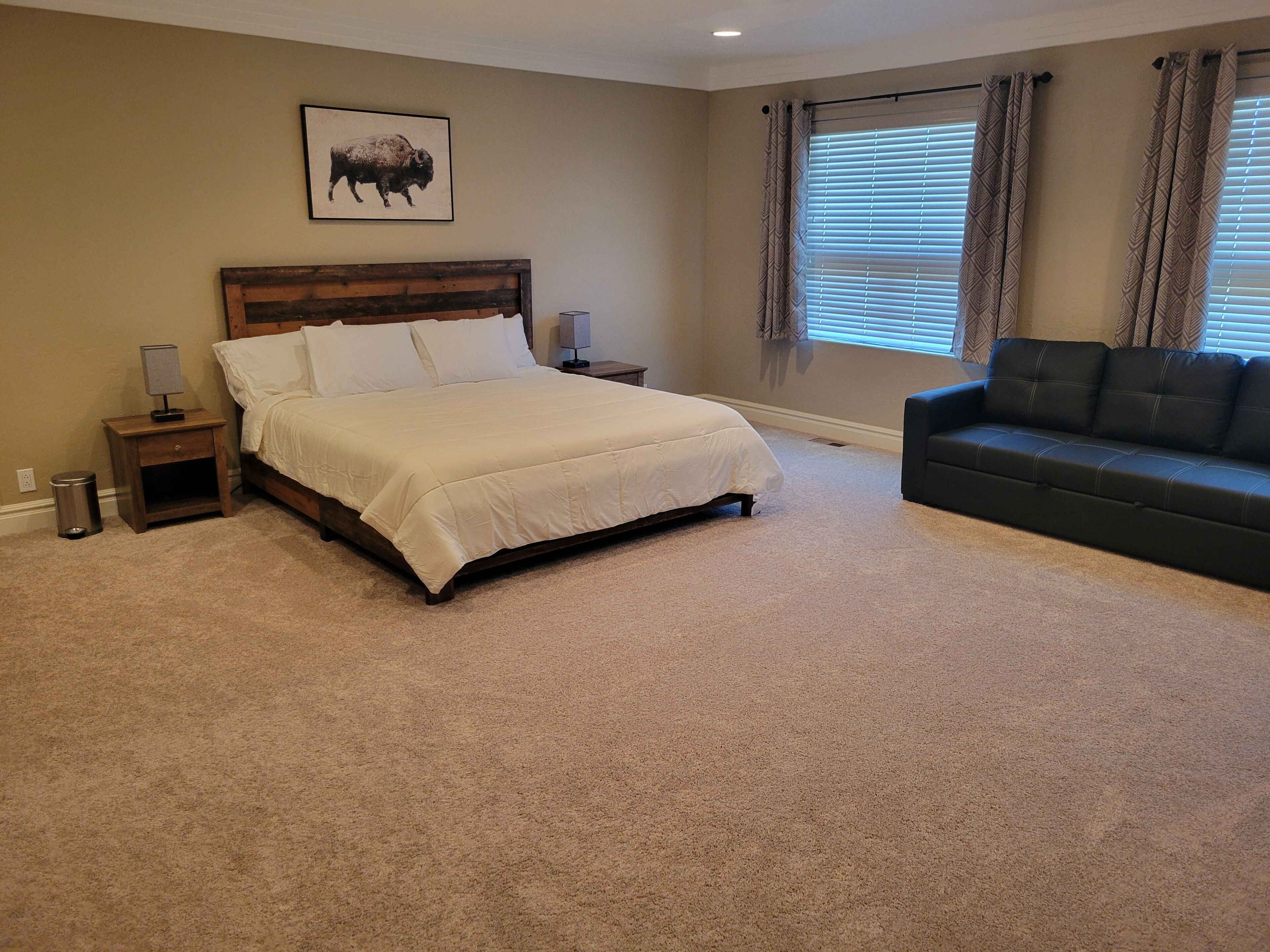 A bedroom with a large bed, a nightstand, a lamp, a couch, and a window with curtains.