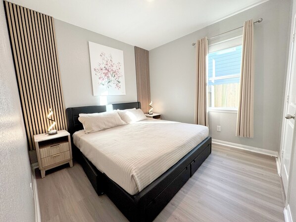 Une chambre bien rangée, avec un lit, des tables de chevet et une fenêtre avec des rideaux.