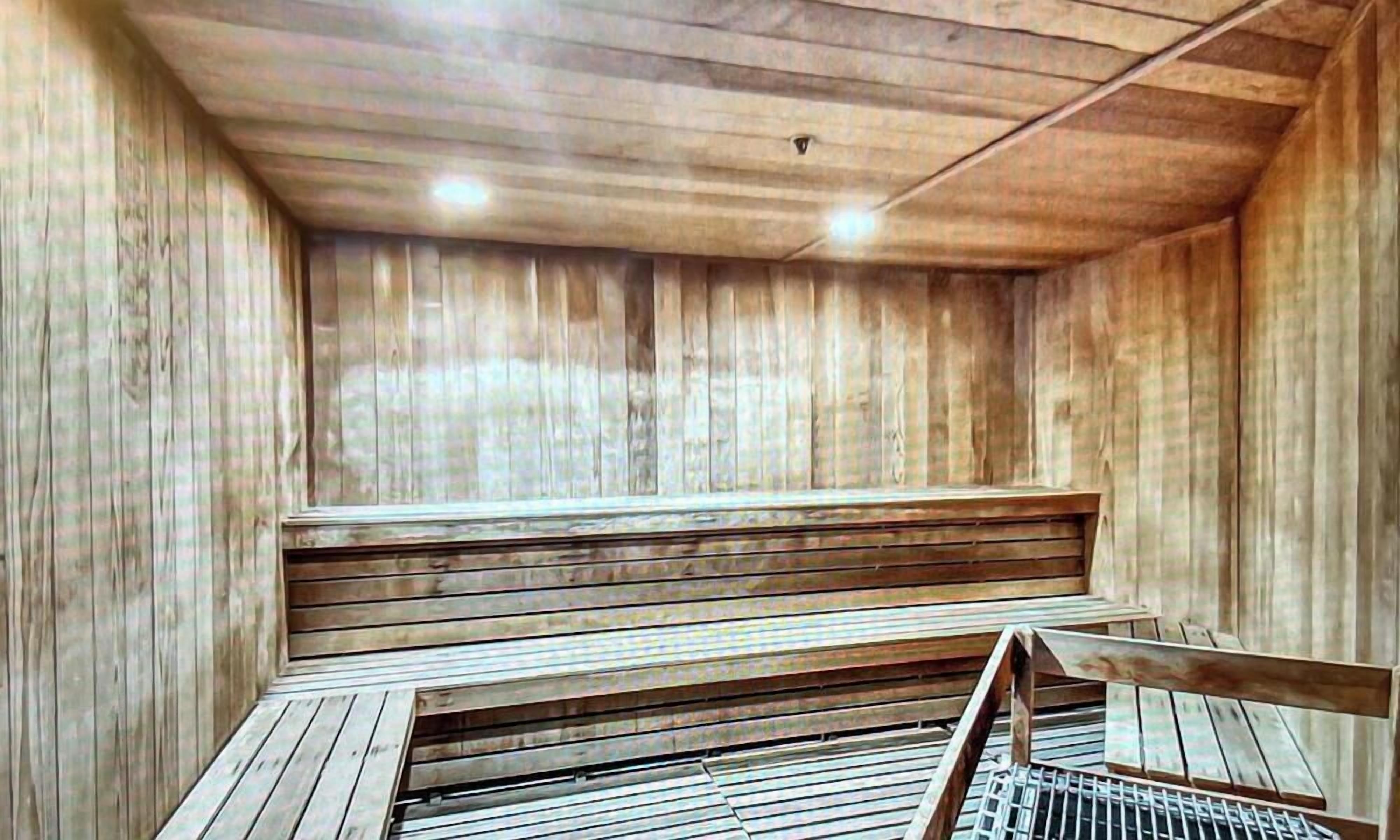 A sauna room with wooden walls and benches, a sloped ceiling, and a metal grate at the bottom.