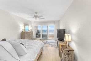 A bedroom with a bed, a TV, a lamp, a dresser, and a view of the ocean.