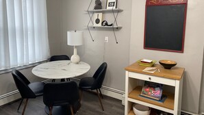 Une pièce moderne avec une table ronde, des chaises noires, une lampe blanche, un tableau noir et une étagère remplie de livres et de bols.