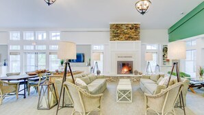 A spacious living room with a fireplace, wicker furniture, and large windows. - Beachwoods - 2BR/3BA - Great Pools and Amenities! (Kitty Hawk)