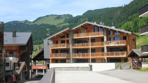 Un immeuble en bois à plusieurs étages, doté de balcons, qui se dresse sur un fond de paysage montagneux.