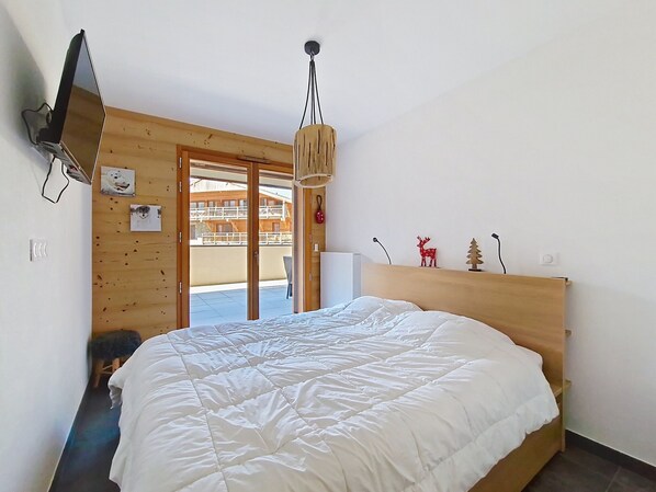 A bedroom with a large bed, wooden walls, a ceiling light, and a view of a building outside.