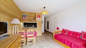 A cozy room with a wooden interior, a TV, a desk with a computer, a bed with red bedding, and a hanging light fixture. - Croix de Savoie CX22 CENTER & VIEW 2 Pers. (Châtel)