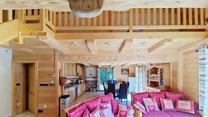 L’intérieur d’un chalet en bois comprend un coin repas, une cuisine et un espace salon confortable agrémenté de coussins roses.