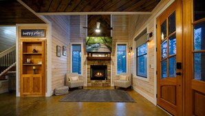 A cozy cabin interior with a fireplace, wooden walls, and a staircase leading to a loft.