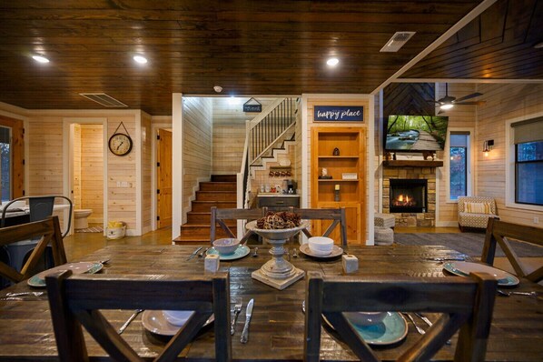 A cozy wooden interior with a dining area, a staircase, a fireplace, and a 'happy place' sign.