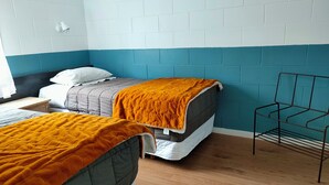 Ein Zimmer mit zwei Betten, einem Metallstuhl und einer weißen Ziegelwand.
