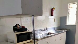 Eine Küche mit weißen Schränken, einer Edelstahl-Spüle, einer Mikrowelle und einer Holzausziehtafel.