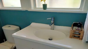 Ein Badezimmer mit einem weißen Waschbecken, einer Toilette und einem Fenster mit einem Blumentopf.