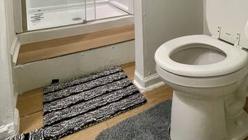 Een badkamer met een douchecabine, toilet en een klein plankje met toiletartikelen.