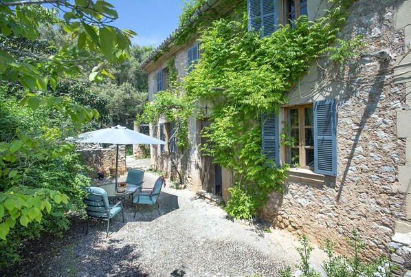 A courtyard with a table and chairs, surrounded by stone walls and greenery.