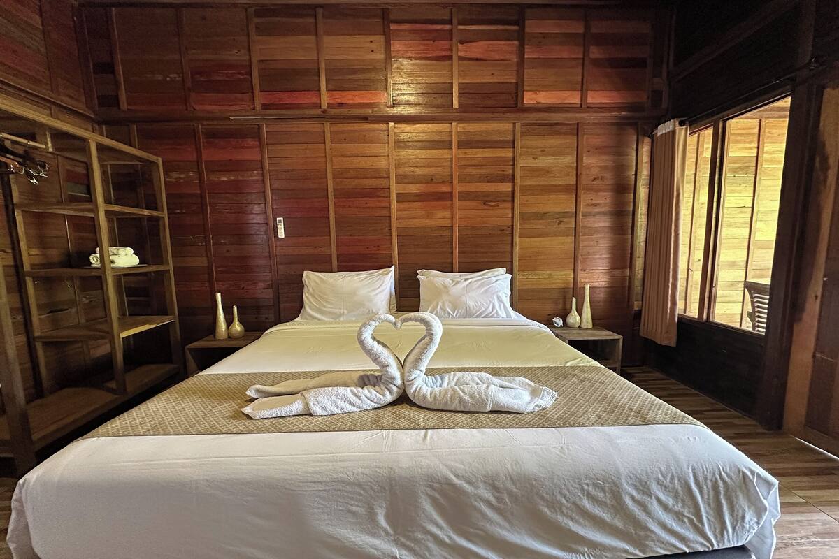 A wooden-paneled room with two beds, a wooden wardrobe, and a large window.