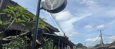 A sign for "MAHAYANA GUEST HOUSE" with a traditional design, located on a street with buildings and power lines in the background.
