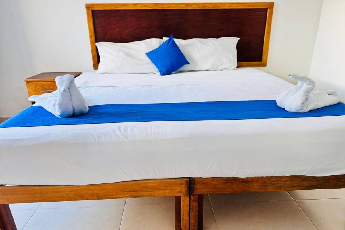 A neatly made bed with white linens, a blue bedspread, and two white towels folded at the foot of the bed.