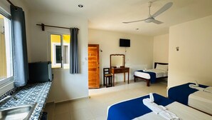Ein Hotelzimmer mit Küchenzeile, einem Bett, einem Schreibtisch mit Stuhl, einem Spiegel und einem Deckenventilator.