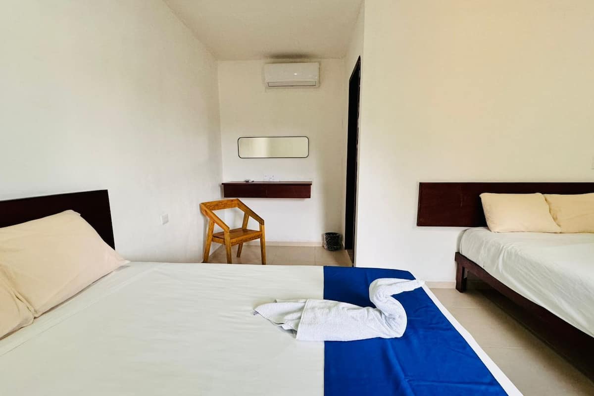 A hotel room with two beds, a wooden chair, a desk, and a mirror.
