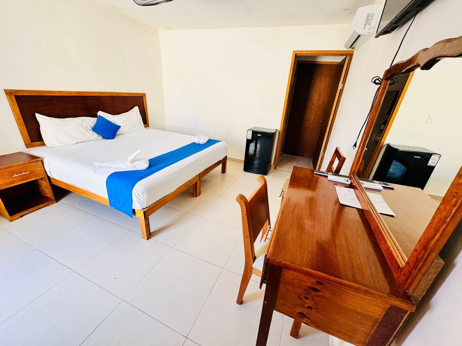 A hotel room with a bed, bedside table, wooden desk, chair, and a mirror.