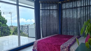 Een slaapkamer met een groot raam, een balkon en een bed met een beddeken met een patroon.