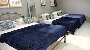 Een hotelkamer met twee bedden, elk met een blauwe spreideken en decoratieve kussens. Er hangen ingelijste foto's aan de muur en er is een spiegel boven de bedden.