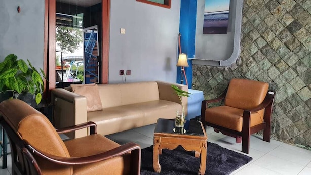 Een woonkamer met een beige bank, twee bruine fauteuils, een kleine houten salontafel en een potplant.