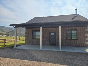Una casa de ladrillo con porche cubierto, chimenea y puerta con ventana.