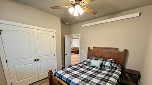 A bedroom with a wooden bed, a ceiling fan, and white double doors. - Charming cabin with WiFi - perfect for a cozy getaway (Smoot)