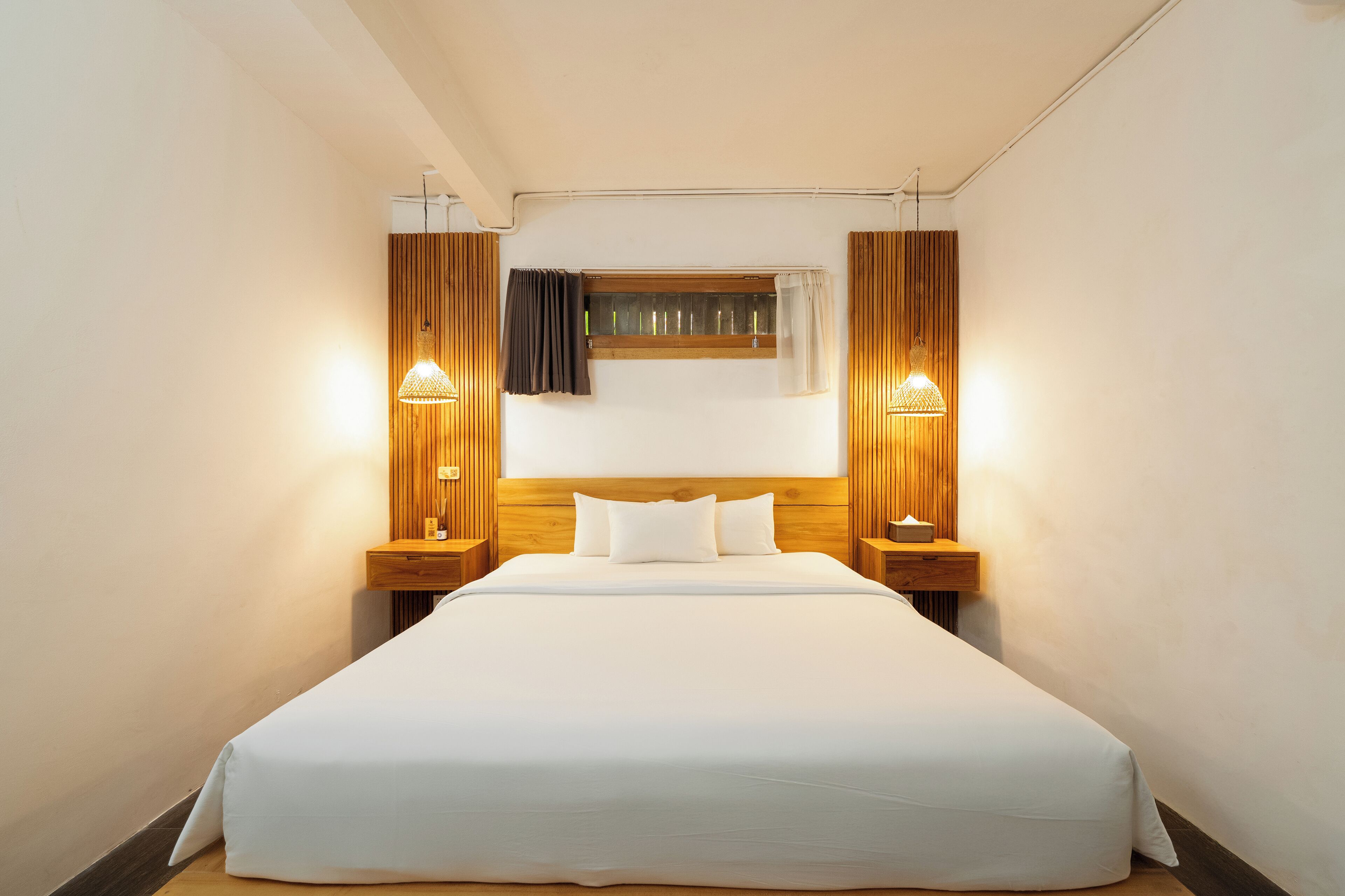 A hotel room with a large bed, wooden headboard, two bedside tables, and a window with curtains.