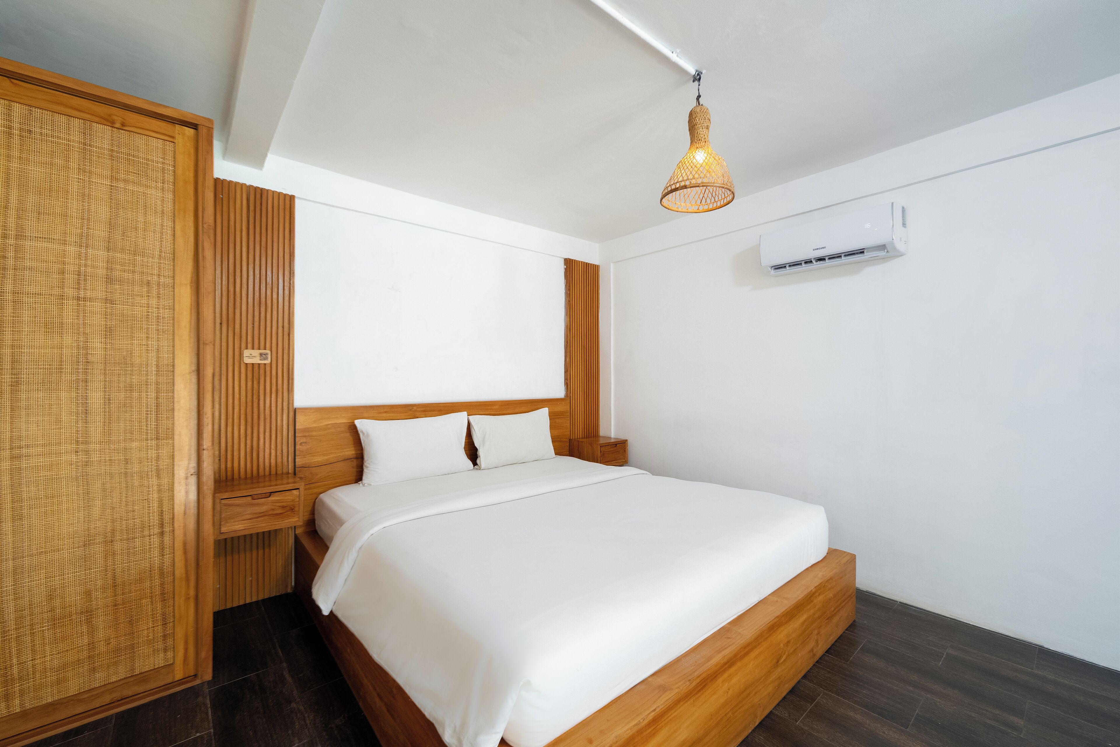Une chambre à coucher moderne avec une tête de lit en bois, un grand lit, une table de chevet et un luminaire suspendu.