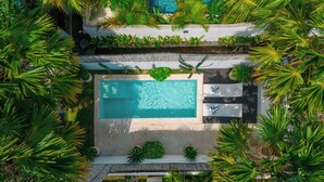 An aerial view of a resort with a central swimming pool, surrounded by lush greenery and palm trees.