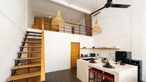 Une cuisine moderne dotée d’un îlot central, d’un escalier en bois et de luminaires suspendus.