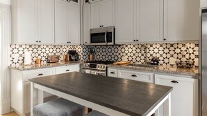 Une cuisine avec des meubles blancs, un îlot central, un four à micro-ondes et un pare-feu décoratif.