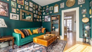 Une pièce avec un mur de couleur turquoise, un canapé vert, une table basse en bois et un tapis à motifs.