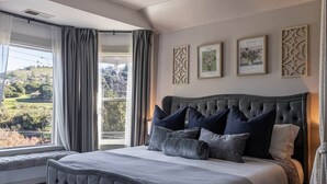 Une chambre avec un grand lit, une vue sur un paysage et des tableaux encadrés au mur.