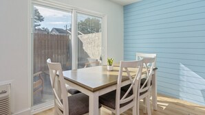A dining area with a table and four chairs, a potted plant, and a view through large windows. - Sunny Haven #623: 1BR Townhome in Fort Walton (Fort Walton Beach)