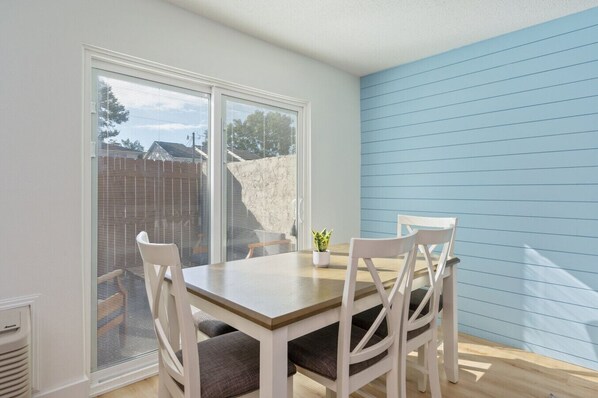 A dining area with a table and four chairs, a potted plant, and a view through large windows.