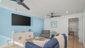 A modern living room with a flat-screen TV, a ceiling fan, a sofa, a coffee table, and a cabinet. - Sunny Haven #623: 1BR Townhome in Fort Walton (Fort Walton Beach)
