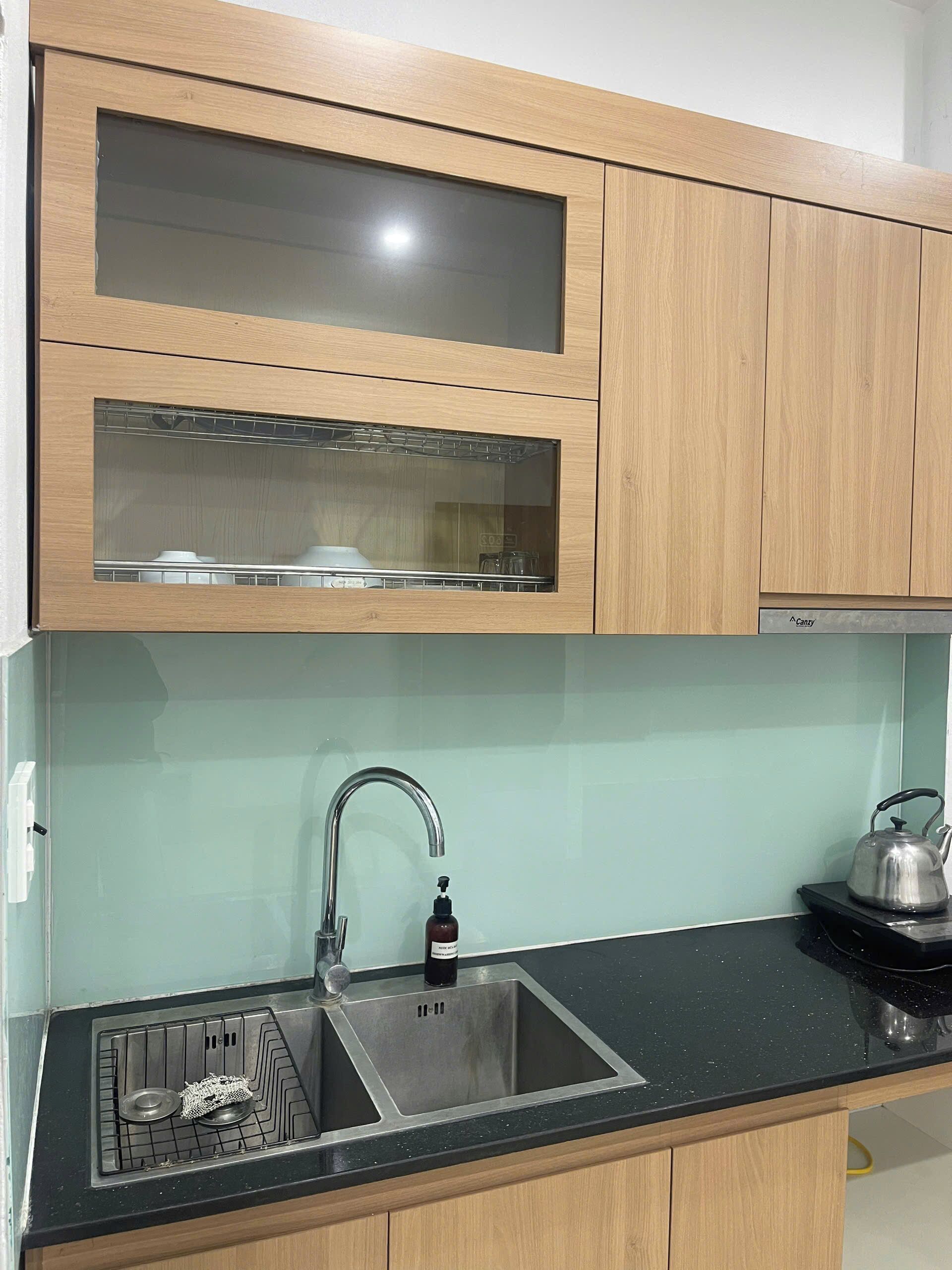 A kitchen with wooden cabinets, a stainless steel sink, and a kettle on the countertop.