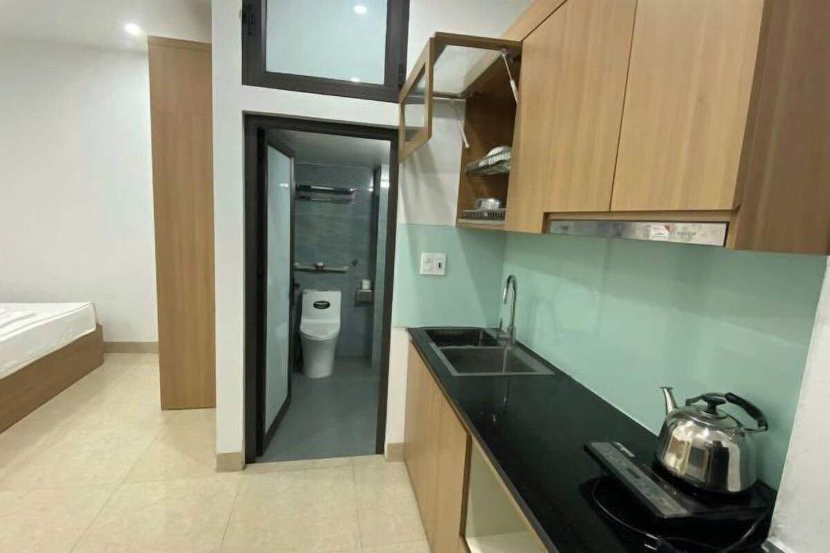 Cocina pequeña con cubierta negra, hervidor y armarios de madera.