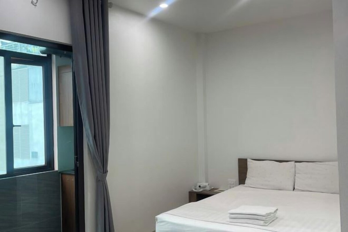Habitación de hotel con cama, mesita de noche, ventana con cortinas y vistas al exterior.