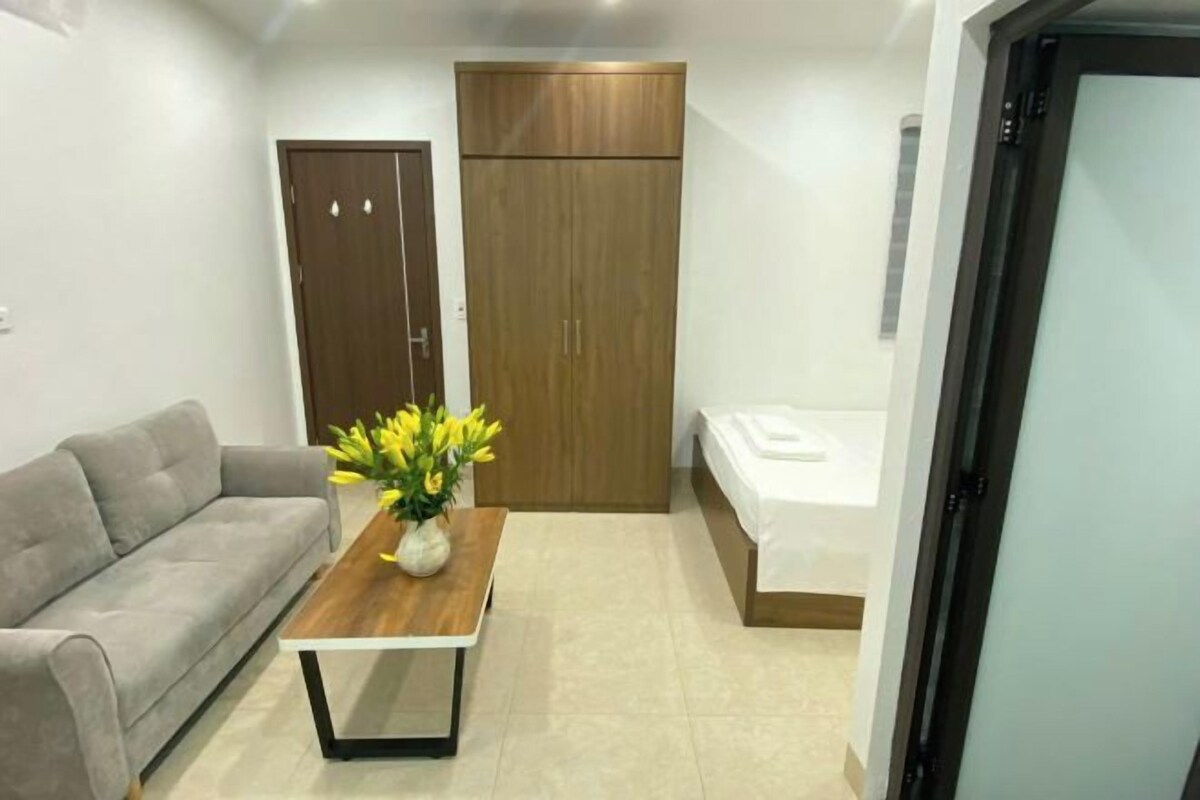 Una habitación compacta con sofá, una mesa de madera con un florero, armario y cama.